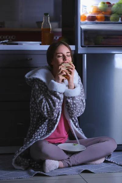 Gyönyörű fiatal nő eszik egészségtelen étel közelében hűtőszekrény éjjel — Stock Fotó
