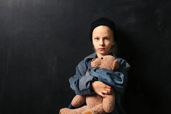 Menina sem-teto com ursinho de pelúcia no fundo escuro — Fotografia de Stock