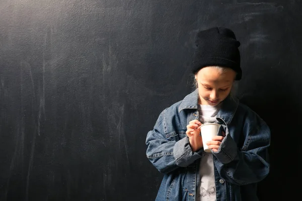 Pequeña sin hogar con taza sobre fondo oscuro — Foto de Stock