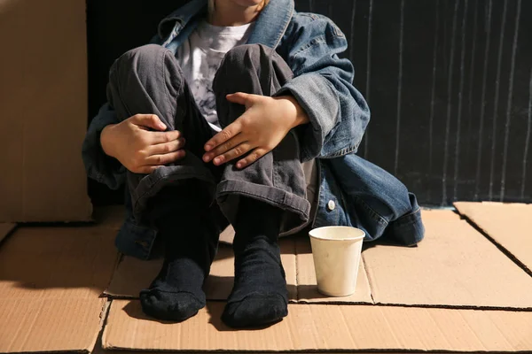 Niña sin hogar sentada en el suelo cerca de la pared oscura —  Fotos de Stock