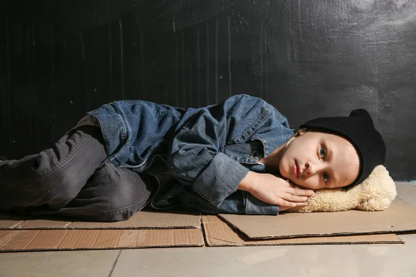 Pequeña sin hogar tumbada en el suelo cerca de la pared oscura — Foto de Stock
