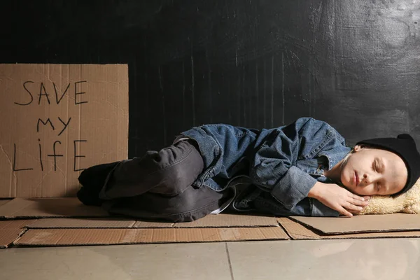 Pequeña sin hogar durmiendo en el suelo cerca de la pared oscura — Foto de Stock