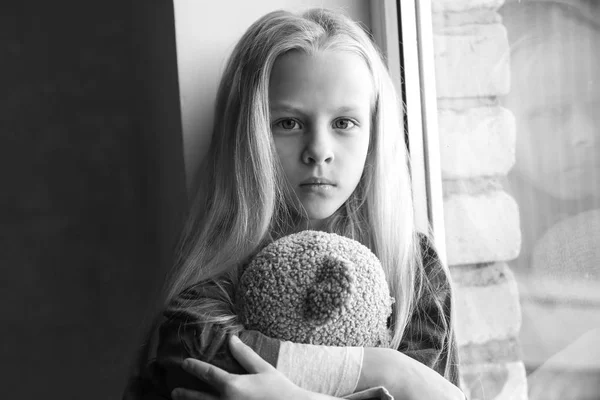 Kleines obdachloses Mädchen mit Teddybär auf Fensterbank — Stockfoto
