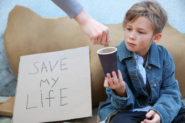 Женщина дает деньги бездомному маленькому мальчику на улице — стоковое фото