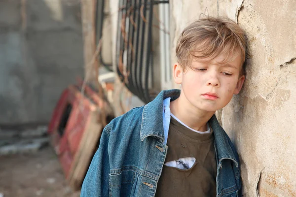 Dakloze kleine jongen in de buurt van de muur buitenshuis — Stockfoto