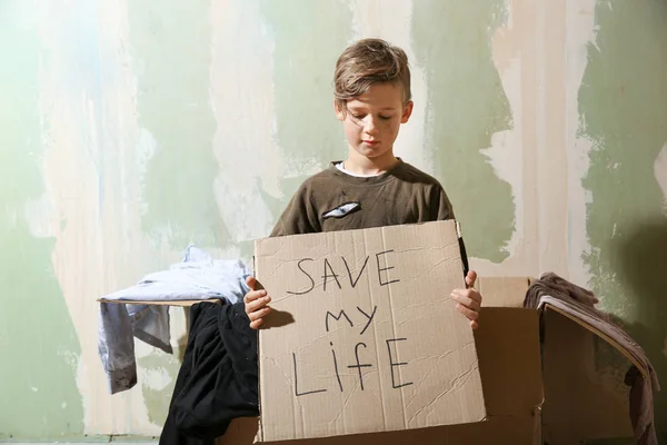 Бездомный маленький мальчик держит кусок картона с текстом спасти мою жизнь в помещении — стоковое фото