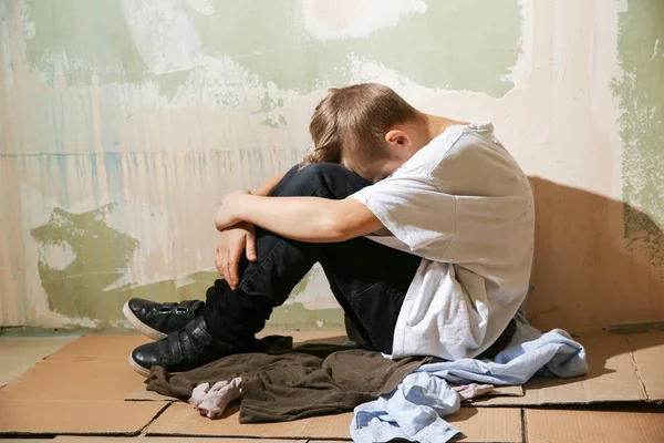 Petit garçon sans abri assis sur le sol près du mur — Photo