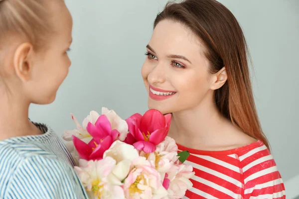Little girl greeting her mother with bouquet of tulips on light background — Stock Photo, Image