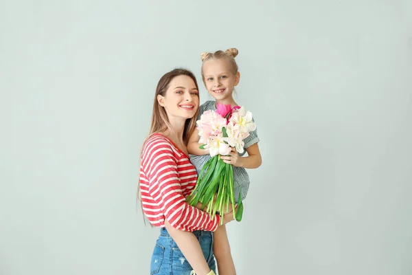 Маленькая девочка и ее мать с букетом тюльпанов на светлом фоне — стоковое фото