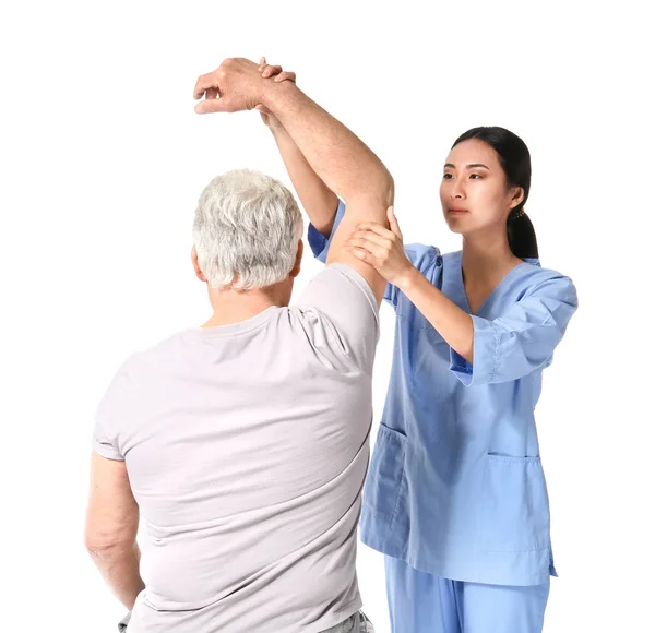 Joven fisioterapeuta asiática trabajando con un hombre maduro sobre fondo blanco —  Fotos de Stock