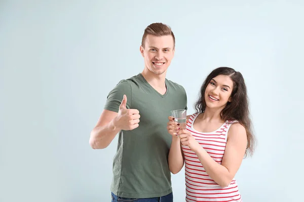 Junges Paar mit Glas Wasser auf hellem Hintergrund — Stockfoto