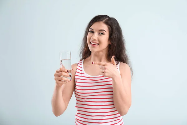 Mooie jonge vrouw met glas water op lichte achtergrond — Stockfoto