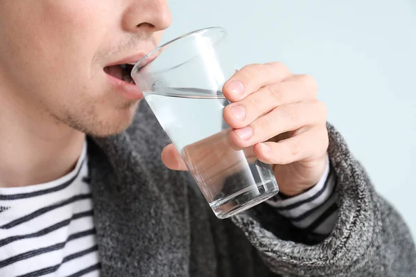 Knappe jonge man drinken water op lichte achtergrond, close-up — Stockfoto
