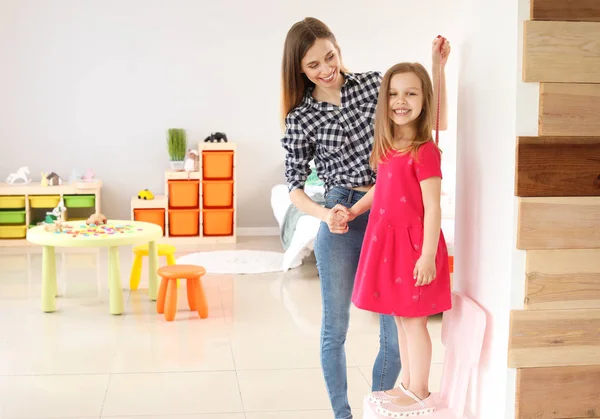 Joven madre midiendo la altura de su pequeña hija en casa — Foto de Stock