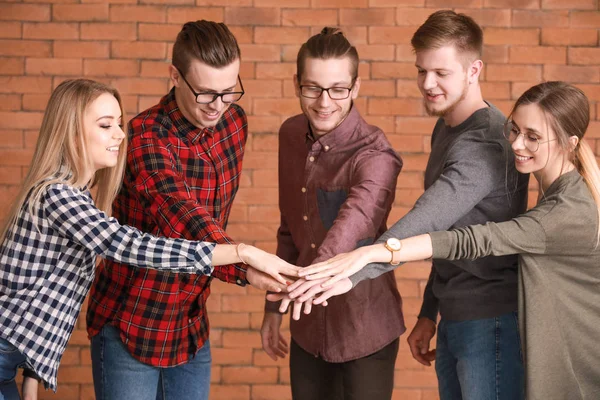 Grupo de jóvenes empresarios que ponen las manos juntas sobre un fondo de ladrillo — Foto de Stock