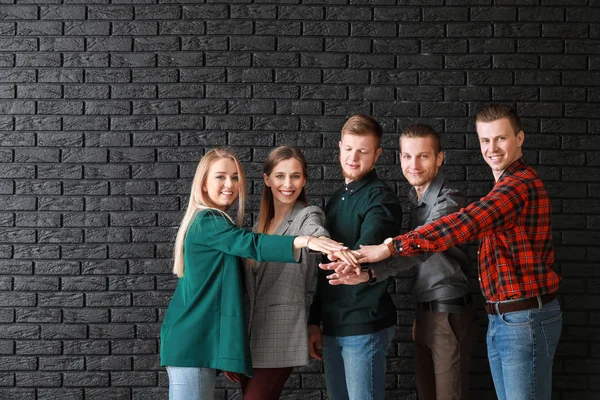 Group of young business people putting hands together on dark brick background — Stock Photo, Image