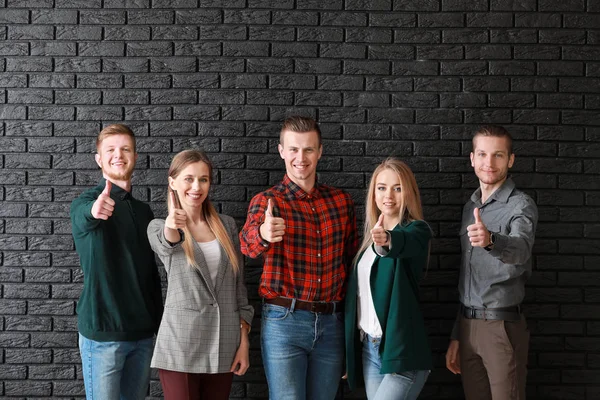 Grupo de jóvenes empresarios mostrando gesto de pulgar hacia arriba sobre el fondo de ladrillo oscuro — Foto de Stock