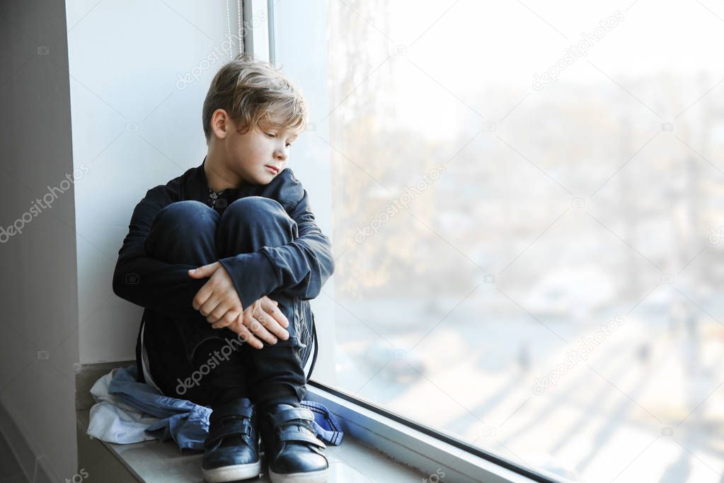 Homeless little boy sitting on window sill indoors
