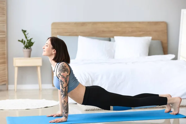 Mulher tatuada bonita praticando ioga em casa — Fotografia de Stock