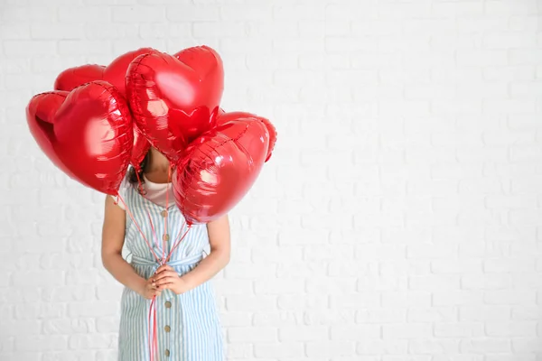 Beautiful young woman with heart shaped air balloons near white brick wall — Stock Photo, Image