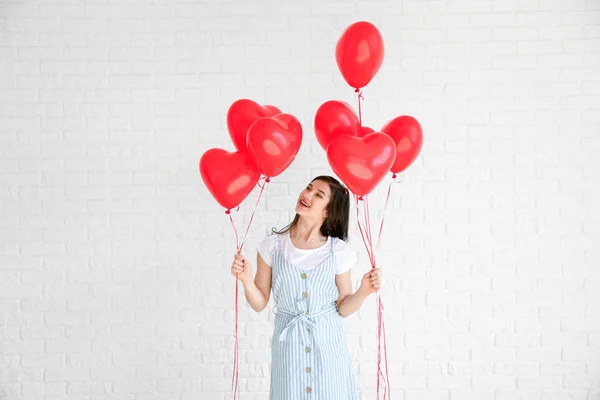 Hermosa mujer joven con globos de aire en forma de corazón cerca de la pared de ladrillo blanco —  Fotos de Stock