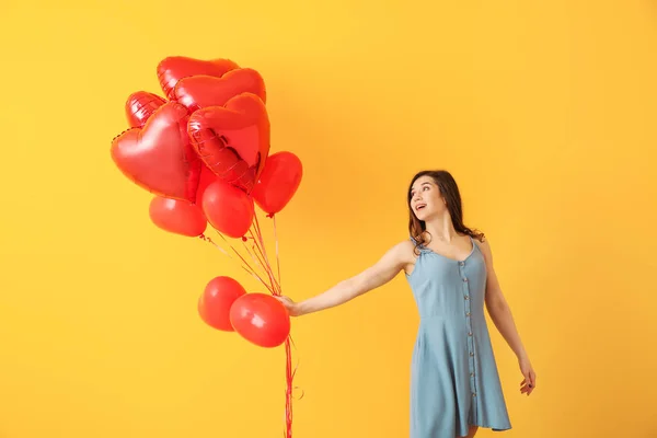 Mooie jonge vrouw met hartvormige lucht ballonnen op kleur achtergrond — Stockfoto
