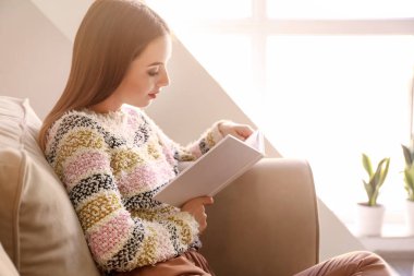 Evde kitap okuyan güzel genç bir kadın.