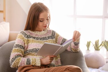 Evde kitap okuyan güzel genç bir kadın.