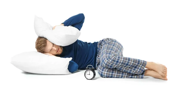 Сонний чоловік прикриває вуха подушкою і відмовляється вставати сигналом будильника на білому тлі — стокове фото