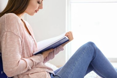 Evde kitap okuyan güzel genç bir kadın.