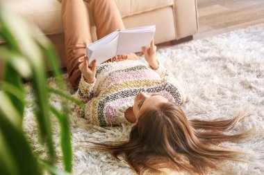 Evde kitap okuyan güzel genç bir kadın.