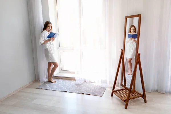 Beautiful young woman reading book near window — Stock Photo, Image