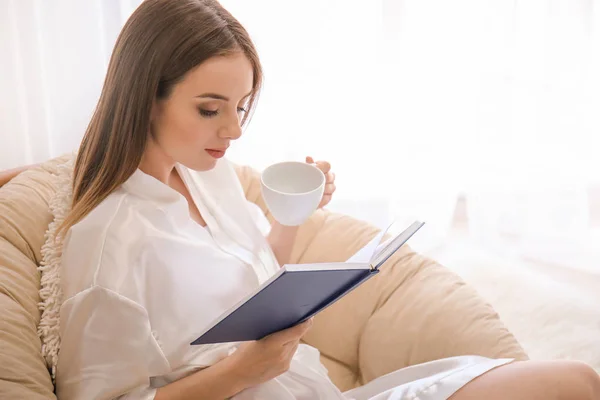 Hermosa joven bebiendo café mientras lee libro en casa — Foto de Stock