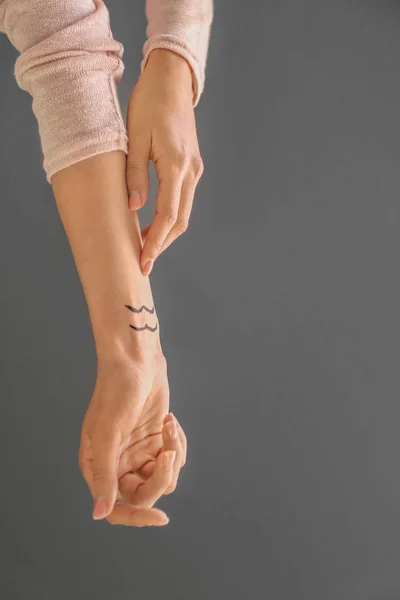 Kvinna med målade Vattumannen stjärntecken på hennes handled mot grå bakgrund — Stockfoto