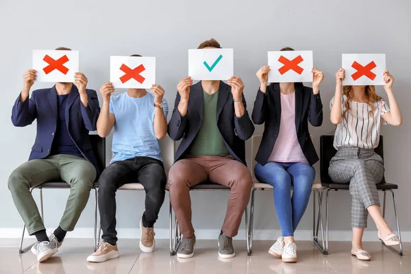 Jóvenes sosteniendo hojas de papel con diferentes marcas mientras están sentados en sillas en el interior. Concepto de entrevista laboral — Foto de Stock