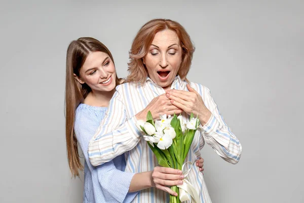 Young woman greeting her mother with bouquet on light background — Stock Photo, Image
