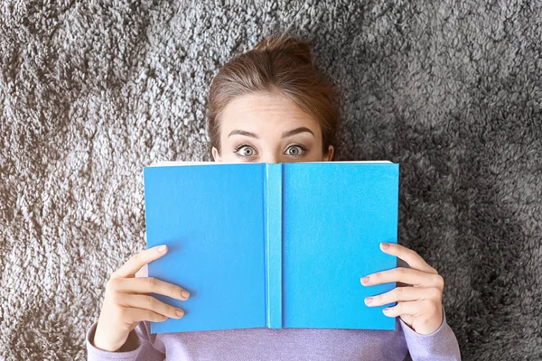 Surprised young woman with book lying on floor, top view — Stock Photo, Image