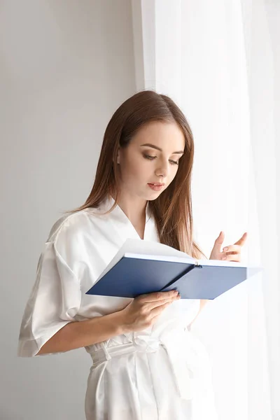 Bella giovane donna lettura libro vicino alla finestra — Foto Stock