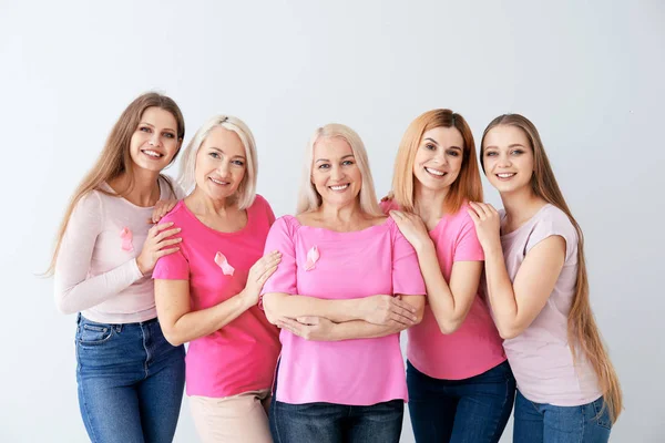 Mooie vrouwen van verschillende leeftijden met roze linten op lichte achtergrond. Borstkanker concept — Stockfoto