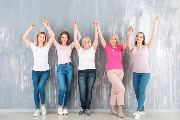 Mulheres felizes de diferentes idades com fitas cor-de-rosa perto da parede cinza. Conceito de câncer de mama — Fotografia de Stock
