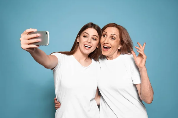 Portrait of happy mother with her daughter taking selfie on color background — Stock Photo, Image