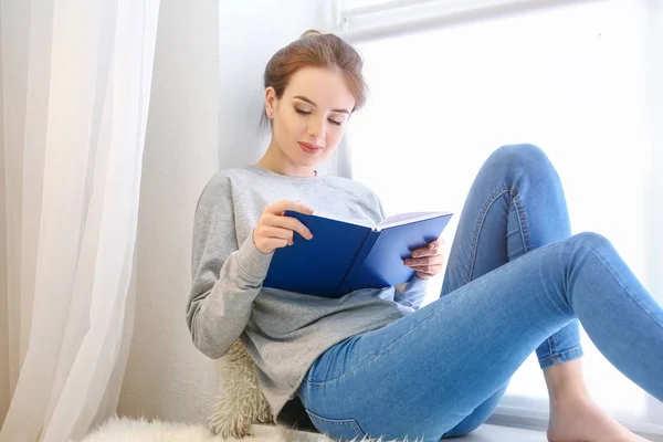 Mooie jonge vrouw lezen boek in de buurt van venster — Stockfoto