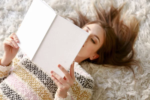 Hermosa joven leyendo libro mientras está acostada en el suelo en casa — Foto de Stock