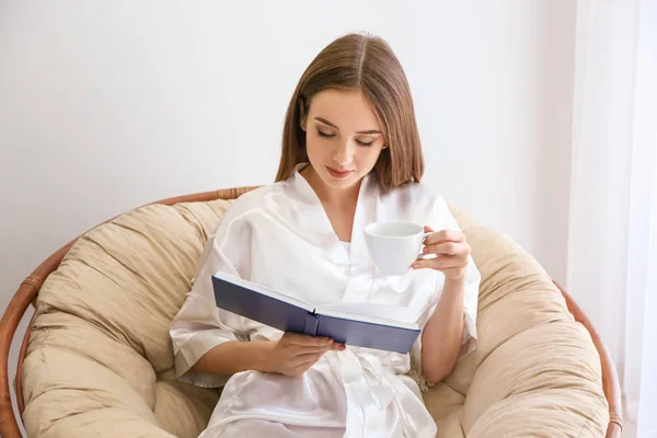 Piękna młoda kobieta czytając książkę i picie kawy w domu — Zdjęcie stockowe