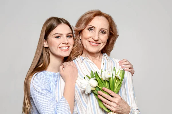 Portrait of mother and her daughter with bouquet on light background — Stock Photo, Image