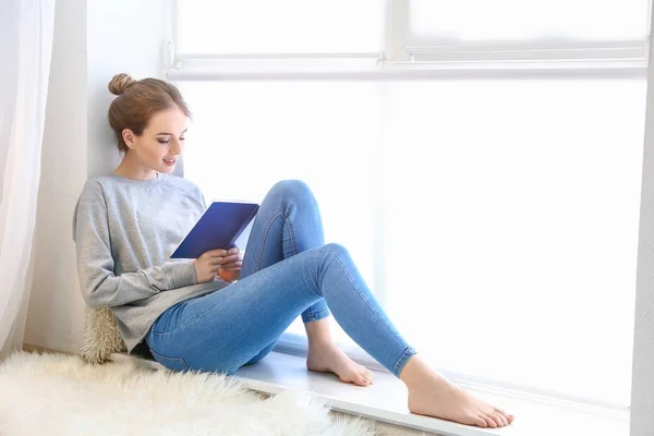 Piękna młoda kobieta czytanie książki w pobliżu okna — Zdjęcie stockowe