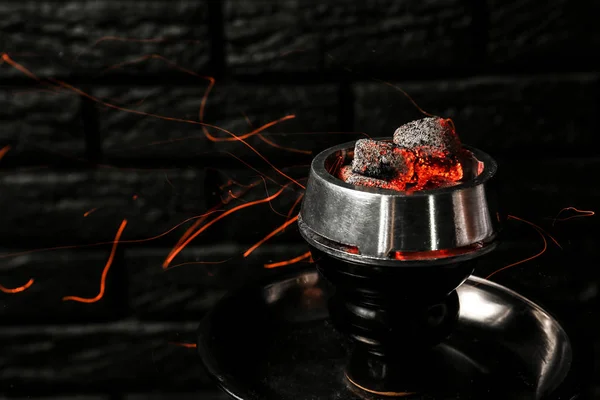 Burning coal for hookah on black brick background