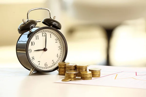 Reloj despertador con monedas y gráfico en la mesa. Concepto de ahorro —  Fotos de Stock