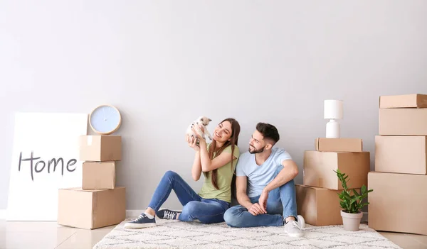 Young couple with belongings and kitten sitting near light wall in their new house — Stock Photo, Image