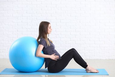 Beyaz tuğla duvar yakınında fitball eğitimi ile güzel hamile kadın